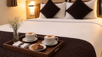 Habitación de hotel con cama, una bandeja con café y galletas, un jarrón con flores y una obra de arte en la pared.