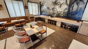 Un comedor moderno con una mesa central, sillas y un banco. En la pared, un cuadro grande que representa un paisaje tropical.