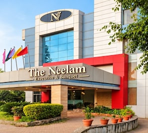 Hotel amb façana moderna, un logotip prominent amb la lletra 'N' i el nom 'The Neelam Executive & Banquet' visible.