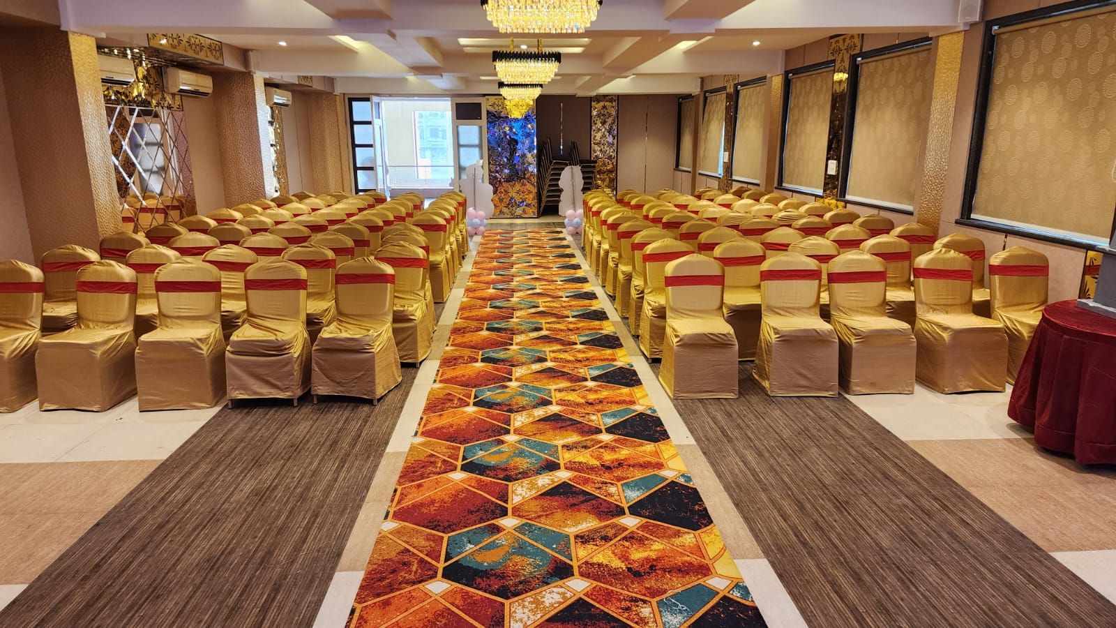 Un salón de conferencias con filas de sillas, un pasillo con alfombra y un escenario al frente.