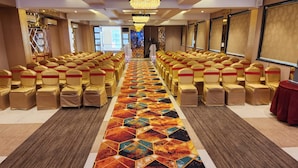 Un salón de conferencias con filas de sillas, un pasillo con alfombra y un escenario al frente.