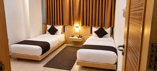 A hotel room with two beds, a nightstand, a lamp, and a wooden door.