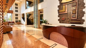 A modern hotel lobby with a reception desk, seating area, and a staircase.