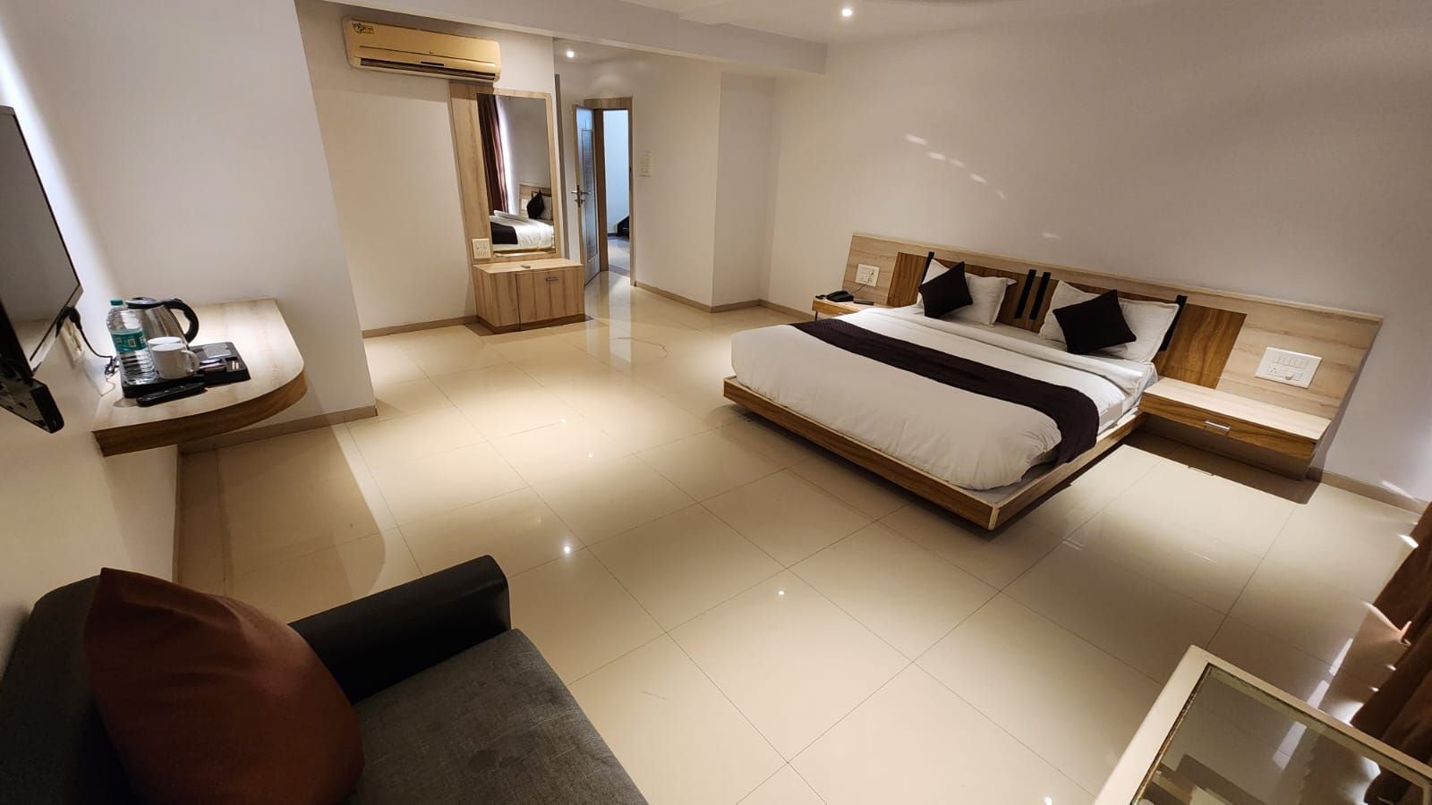 Une chambre d’hôtel moderne dotée d’un grand lit, d’une table de chevet, d’une armoire intégrée et d’un coin salon avec un canapé et un fauteuil.