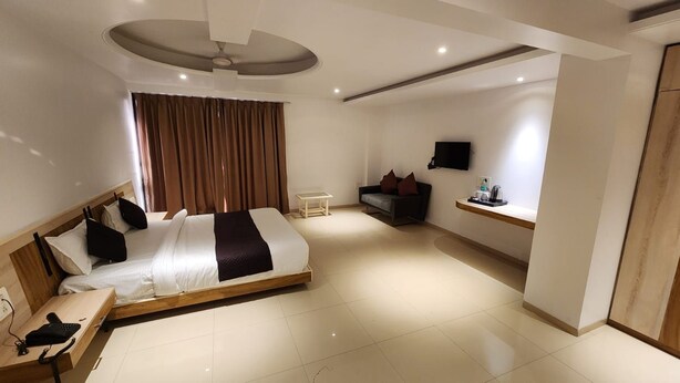 Een moderne hotelkamer met een bed, nachtkastje, een klein bureau met telefoon, een aan de muur bevestigde televisie en een zithoek met een bank en bijzettafeltje.
