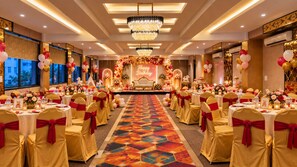 A banquet hall with round tables, chairs with red sashes, a stage with a 'Happy Birthday' sign, and a chandelier. - hotel Neelam Executive  (Rajgurunagar)