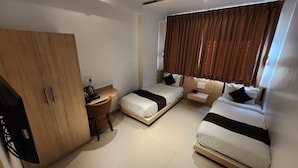Een hotelkamer met een kledingkast, een bureau met stoel, twee bedden en een raam met gordijnen.