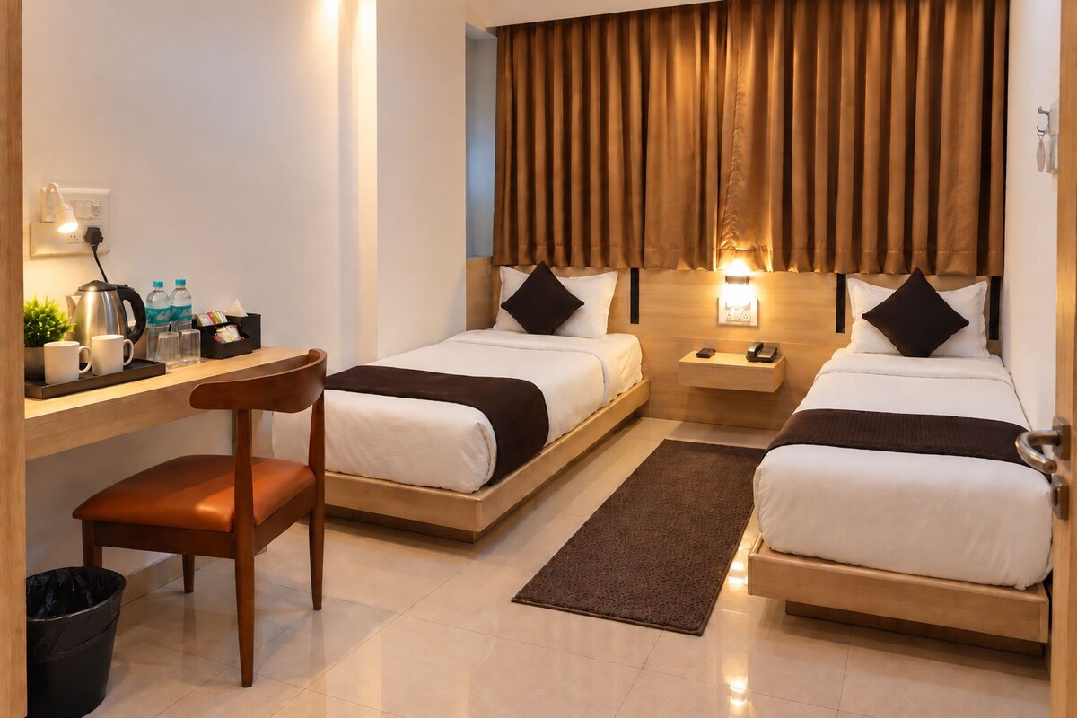 A hotel room with two beds, a desk, a chair, a nightstand, and a window with curtains.