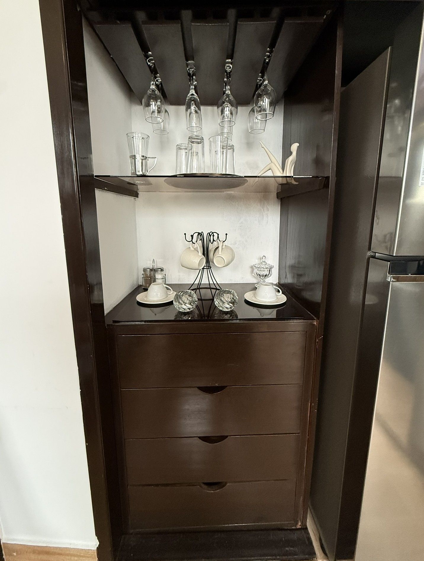 A kitchen with dark cabinetry, a stainless steel refrigerator, and a glassware holder with multiple glasses and cups.