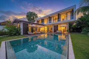 Ein modernes, zweistöckiges Haus mit Swimmingpool und Sitzgelegenheit im Freien.