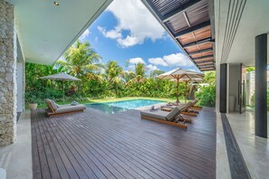 Ein moderner Poolbereich im Freien mit Holzterrasse, Liegestühlen und Sonnenschirmen.