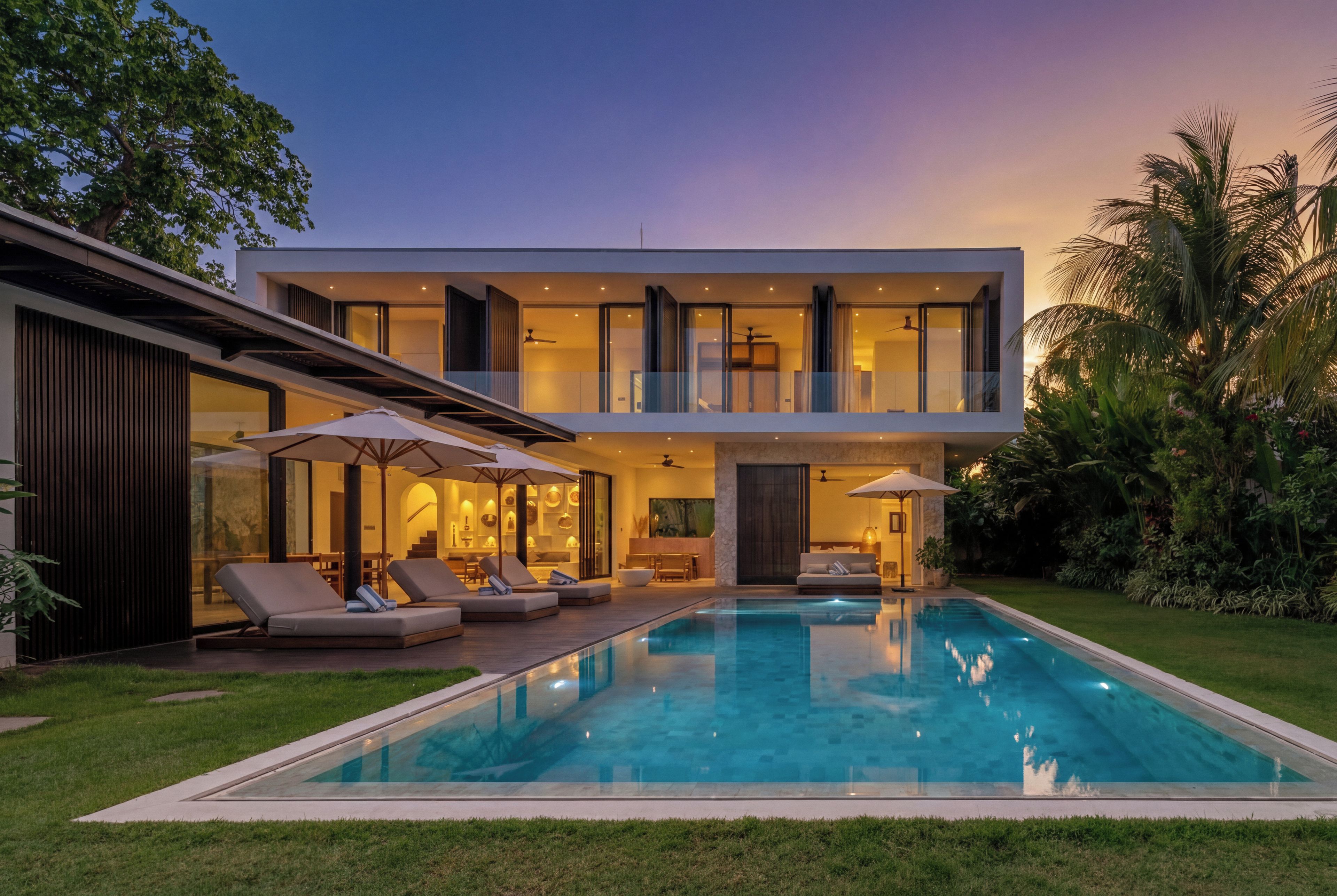 Una casa moderna de dos pisos con piscina, mobiliario exterior y abundante vegetación.