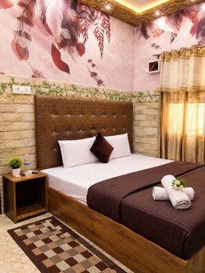 Habitación de hotel con una cama grande, cabecera, mesita de noche, televisor montado en la pared y una ventana con cortinas.
