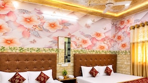 Een hotelkamer met twee bedden, bloemenkunst aan de muur, een plafondventilator en een spiegel.