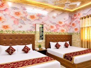Habitación de hotel con dos camas, decoración floral en la pared, ventilador de techo y un espejo.