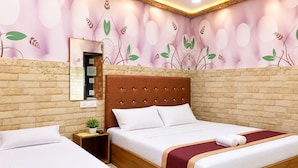 Een hotelkamer met een groot bed, een kleiner bed, een houten hoofdbord, een nachtkastje, een spiegel en een wand met een bloemistisch muurschildering.