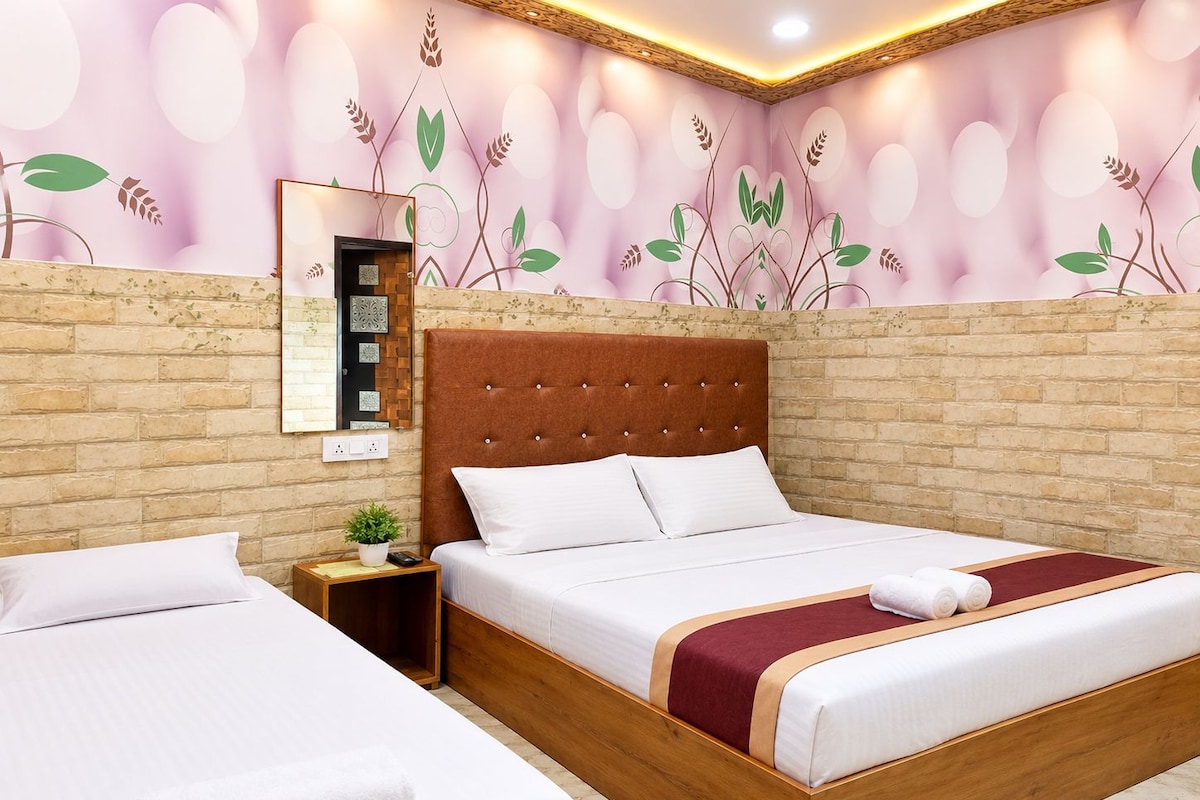 Een hotelkamer met een groot bed, een kleiner bed, een houten hoofdbord, een nachtkastje, een spiegel en een wand met een bloemistisch muurschildering.