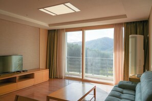 Ein Hotelzimmer mit Flachbildfernseher auf Holzständer, einer Couch, einem Tisch und einer großen Schiebeglasdoor, die auf einen Balkon mit Bergblick führt.