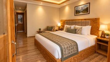 A hotel room with a wooden bed frame, a large bed, a nightstand with a lamp, a wall-mounted painting, and a wooden floor.