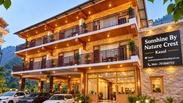 A multi-story hotel with a stone facade, balconies, and a sign advertising 'Sunshine By Nature Crest Kasol'.