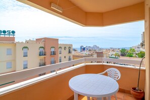 A balcony with a white table and chairs, overlooking a cityscape with buildings and a clear sky. - Apartment in Nerja Near Torrecilla Beach (Nerja)