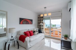 A modern living room with a white sofa, red and black cushions, a glass coffee table, and a painting on the wall. - Apartment in Nerja Near Torrecilla Beach (Nerja)