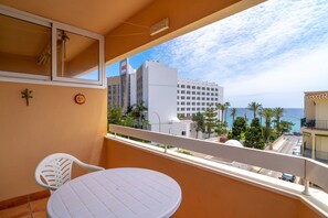 A balcony with a white table and chairs, overlooking a coastal area with buildings and palm trees. - Apartment in Nerja Near Torrecilla Beach (Nerja)