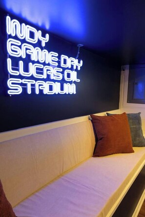 Ein Raum mit einem Neon-Schild, auf dem 'INDY GAME DAY LUCAS C.' steht. Man sieht ein weißes Sofa mit Kissen.