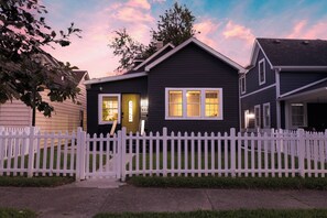 A two-story house with a white picket fence, a front door, and a visible staircase leading to the entrance. - 5 Min to Downtown | Hot Tub • Arcade • Sleeps 11 (Indianapolis)