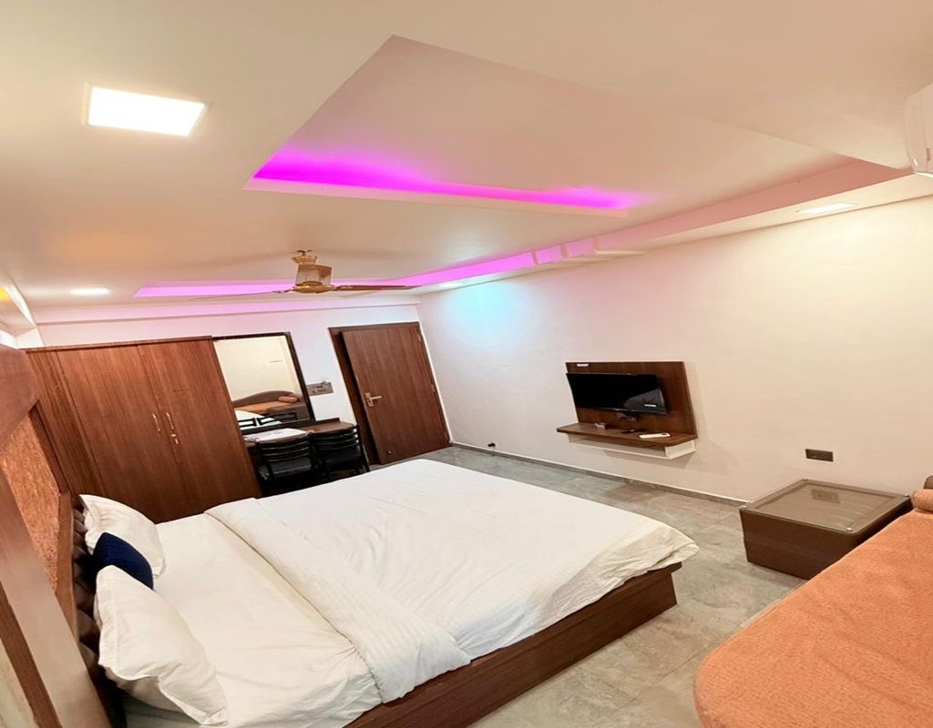 A bedroom with a bed, a wardrobe, a television, and a small table.
