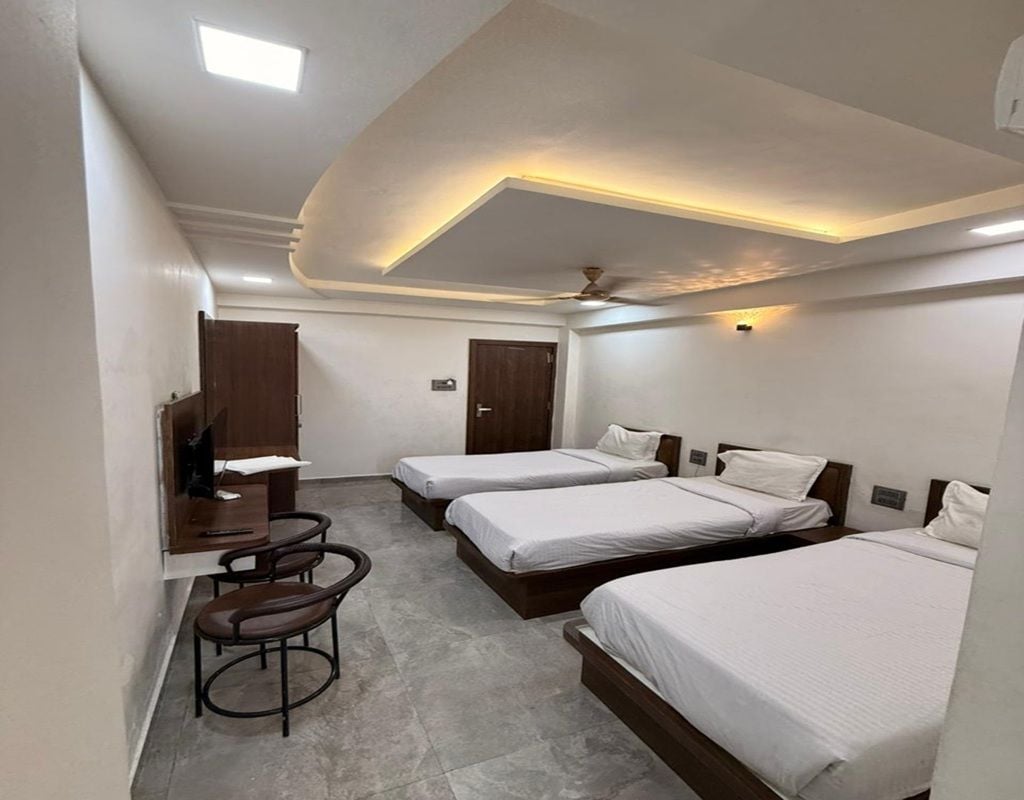 A hotel room with three beds, a desk, and a chair.