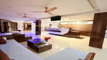 Een hotel receptie met een receptiebalie, een zithoek en een plafondventilator.