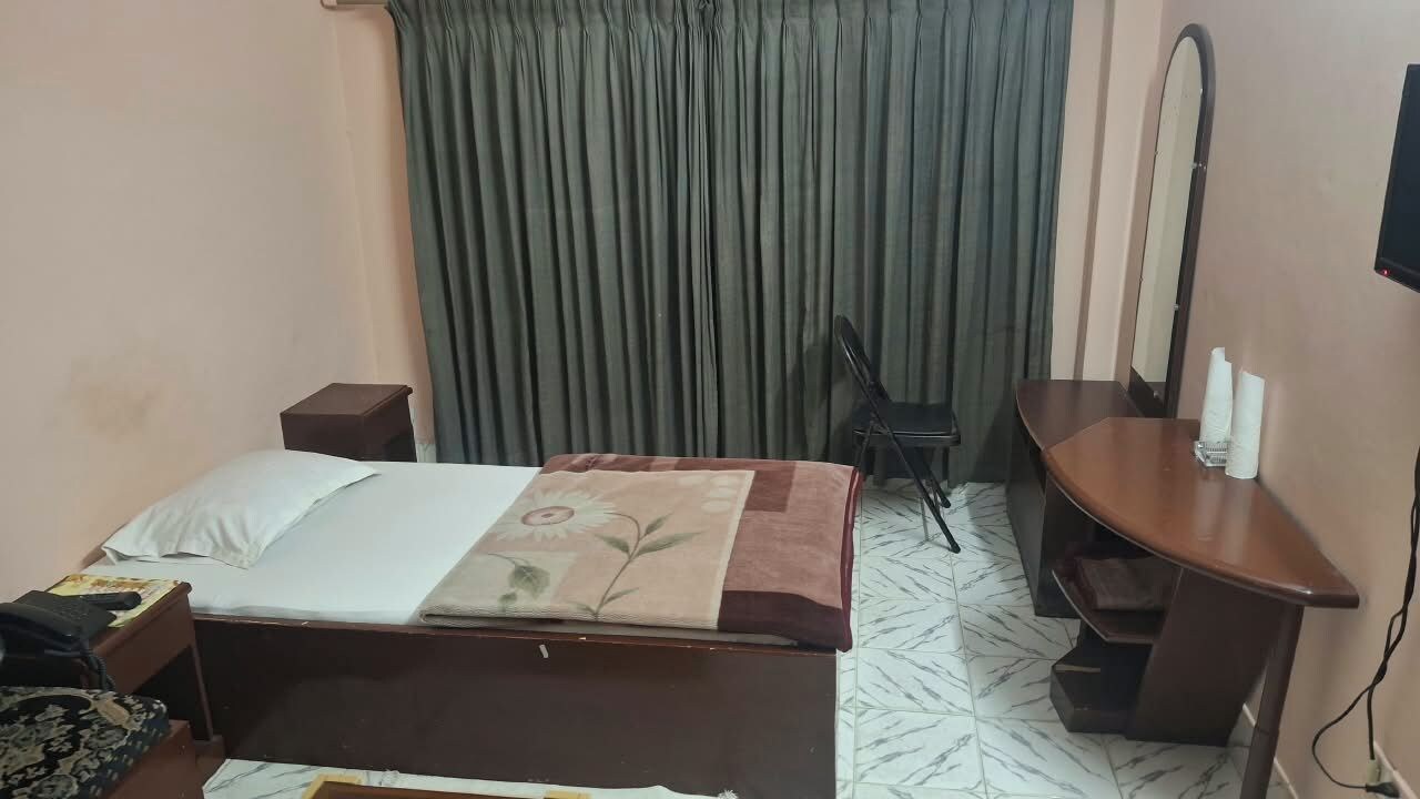 A hotel room with a bed, a desk, a chair, a mirror, and a curtain.