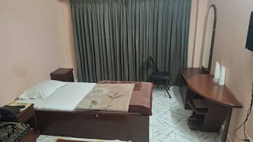 A hotel room with a bed, a desk, a chair, a mirror, and a curtain.