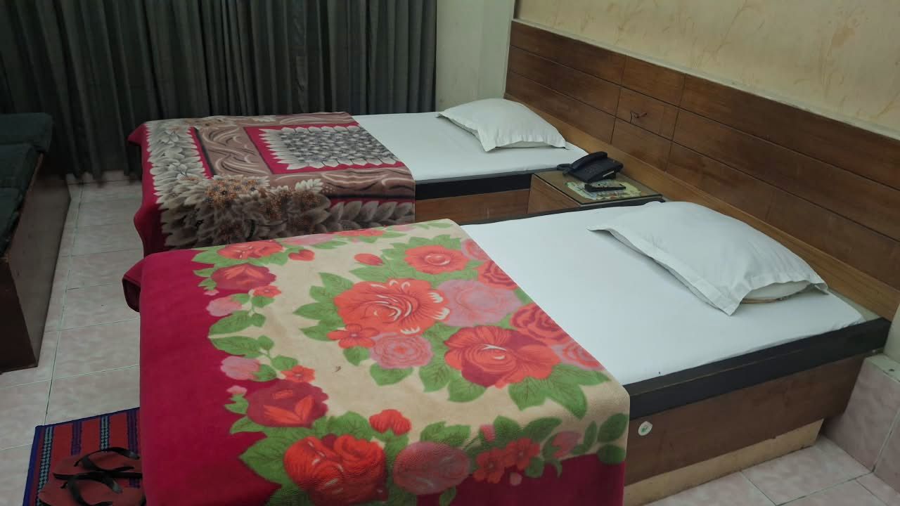 Two single beds with floral bedspreads, a bedside table with a phone, and a curtain in the background.