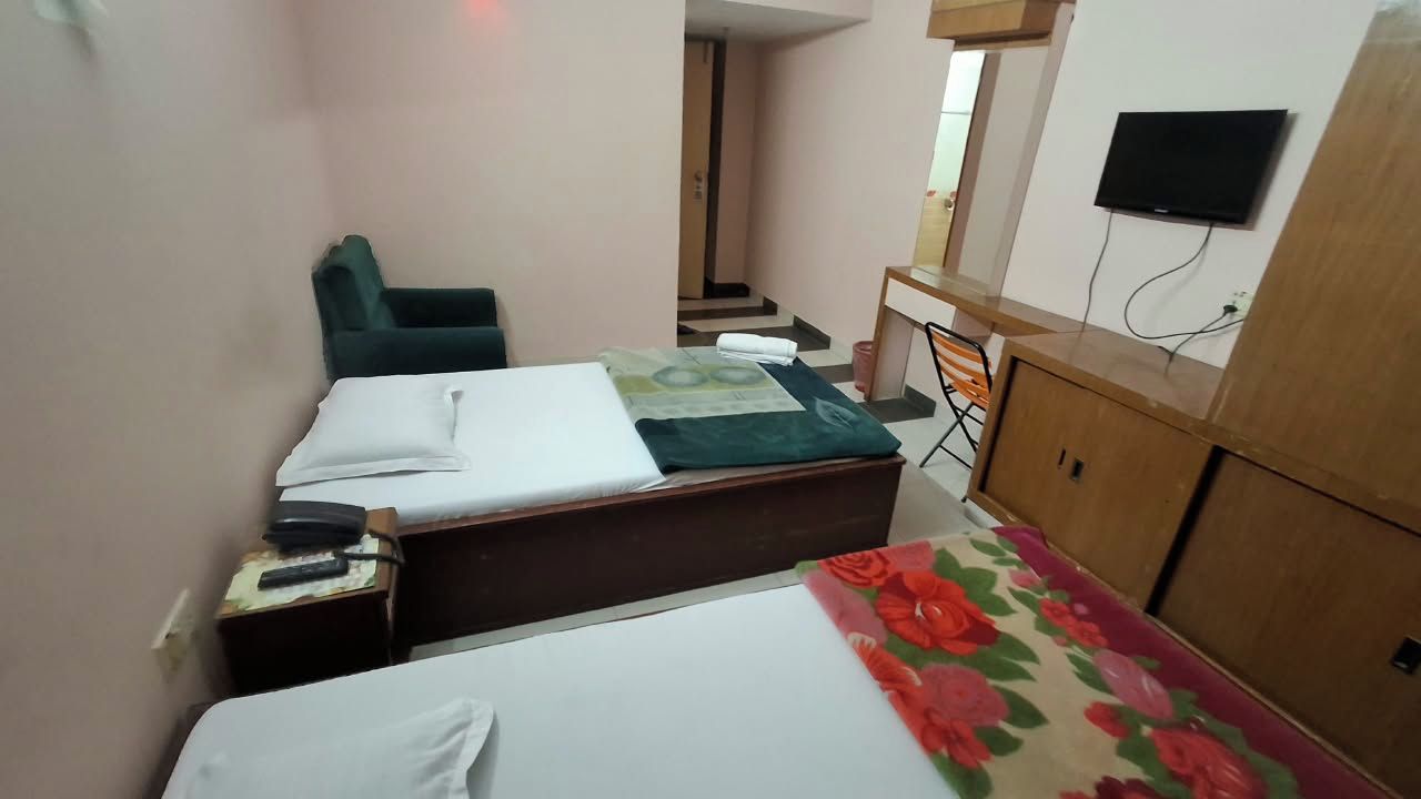 A small hotel room with two beds, a desk, a chair, and a TV.