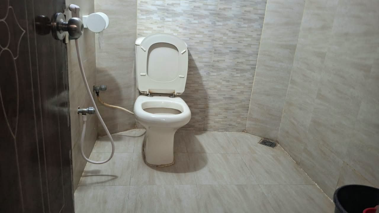 Ein Badezimmer mit Toilette, Dusche und einem Wandarmaturen-Wasserhahn.