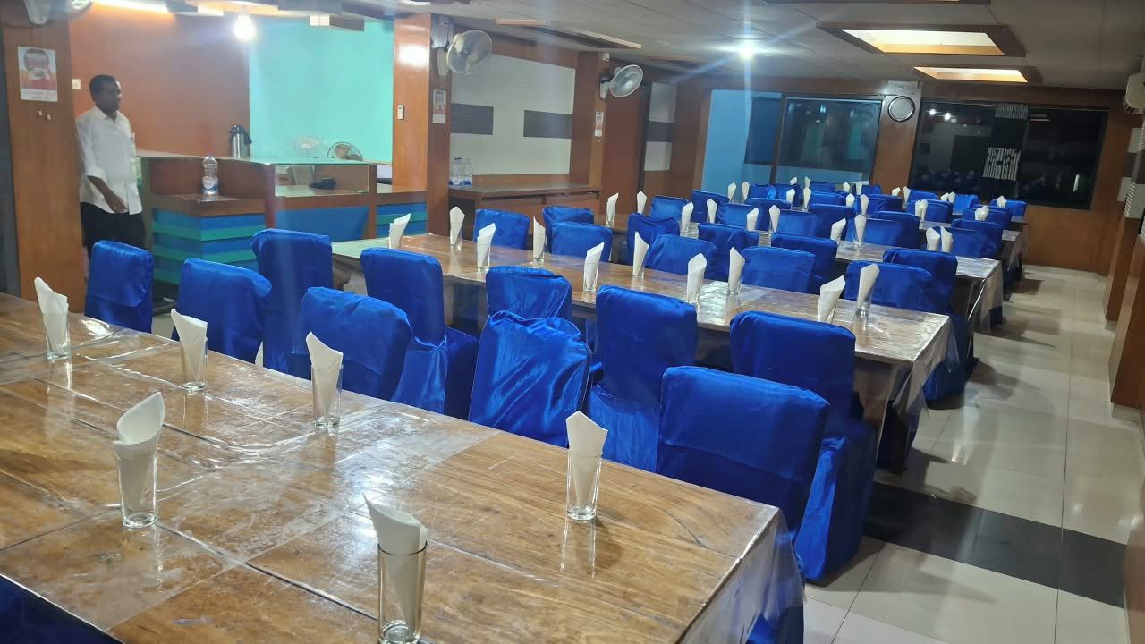 A dining area with multiple tables and chairs, a reception desk, and a person standing near the entrance.