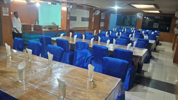 Un área de comedor con varias mesas y sillas, una recepción y una persona de pie cerca de la entrada.
