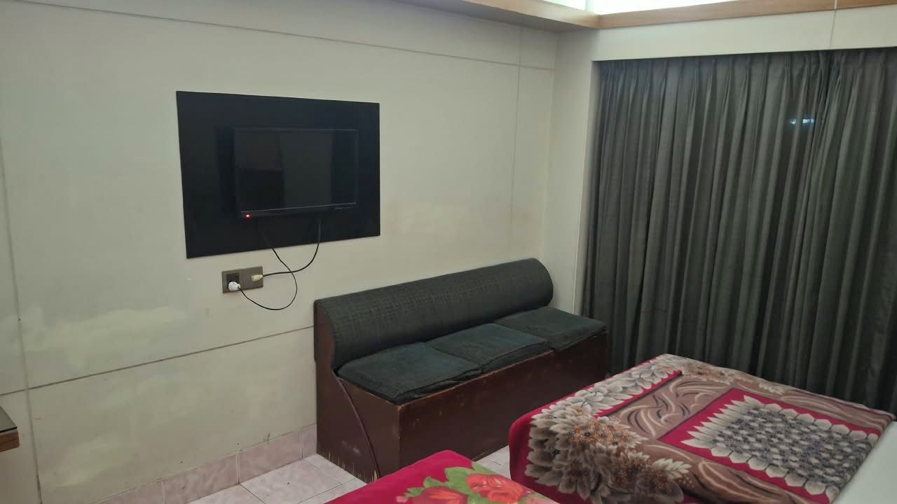 A room with a bed, a sofa, a television mounted on the wall, and a window with curtains.