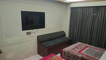 A room with a bed, a sofa, a television mounted on the wall, and a window with curtains.