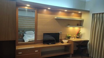 Una habitación de hotel con cama, televisión, escritorio con silla y espejo.