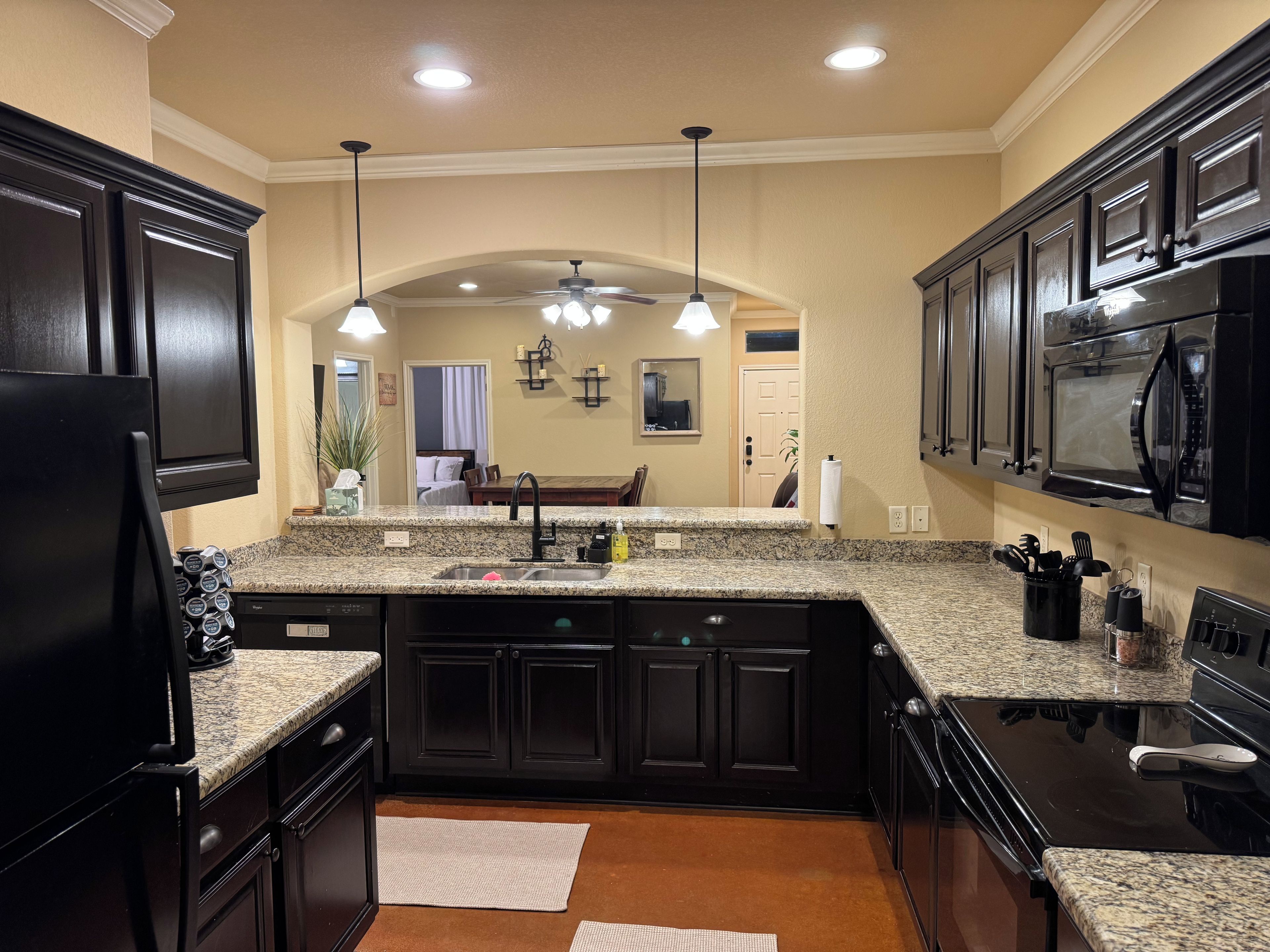 A kitchen with dark cabinetry, granite countertops, a black refrigerator, and a microwave.