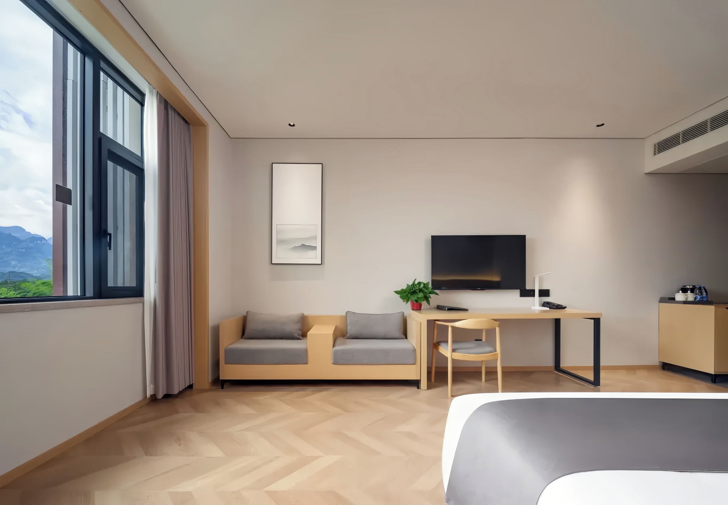 A modern hotel room with a bed, a desk, a sofa, a TV, and a window with a view of mountains.