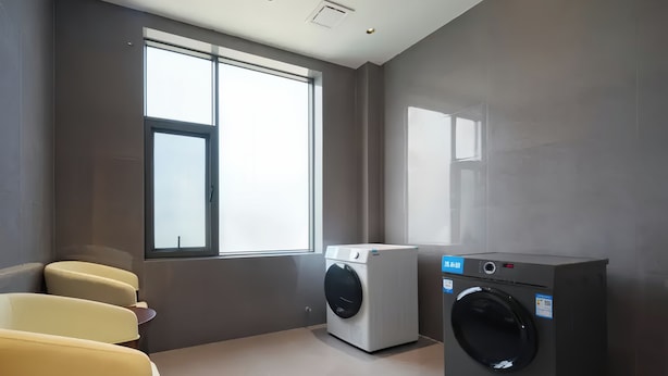 A laundry room with a washing machine and dryer, a window with natural light, and a yellow chair. - Tianmen Skyview Hotel (Zhangzhou)