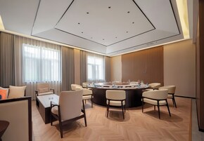 Una sala de conferencias moderna con una mesa redonda, varias sillas y un ventanal con cortinas.