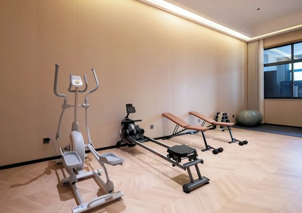 A gym with exercise equipment including a rowing machine, a bench, and dumbbells.