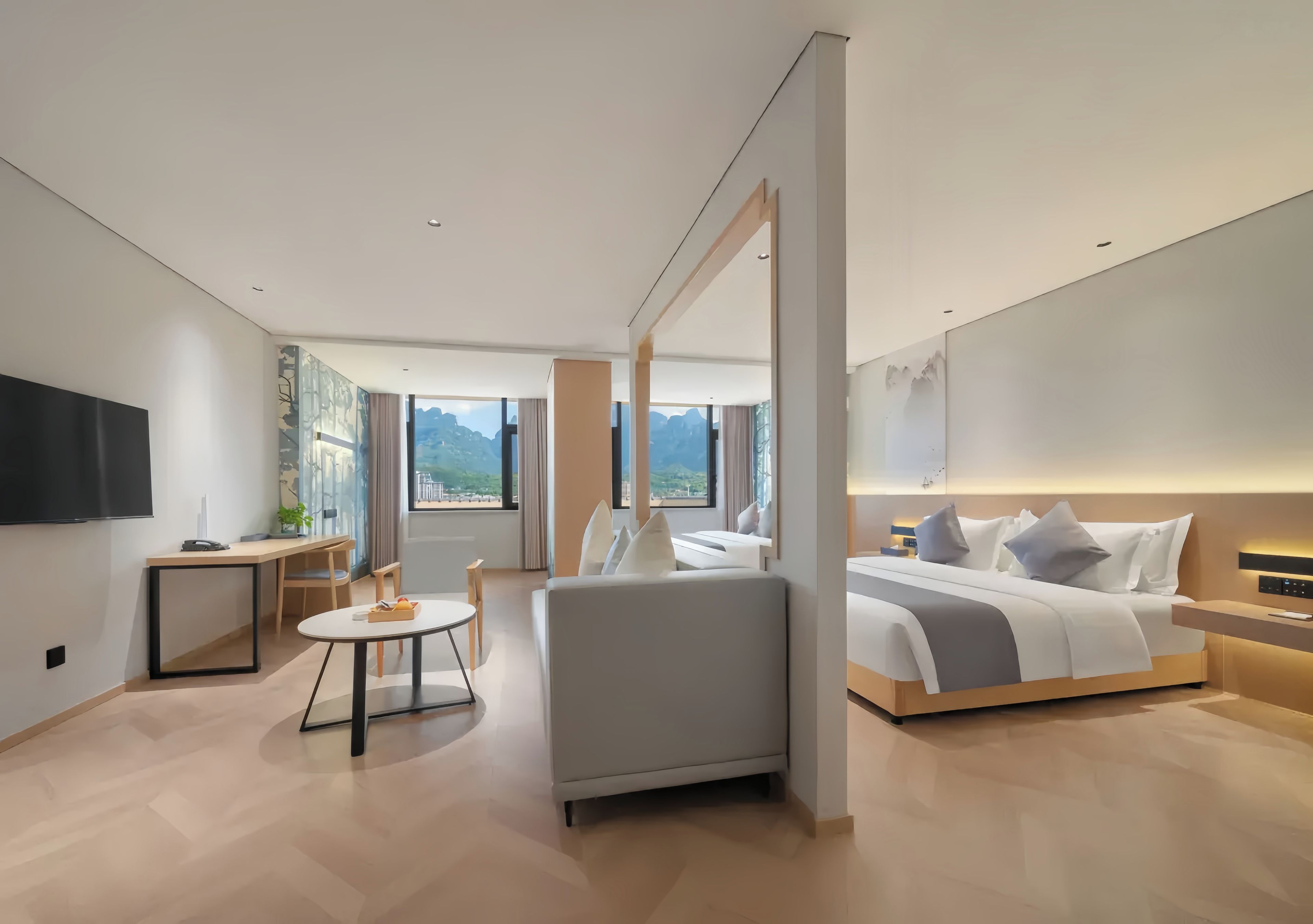 Quarto de hotel moderno com cama, área de estar, mesinha e televisão.