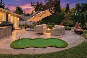 Um quintal com putting green, móveis de exterior e churrasqueira.