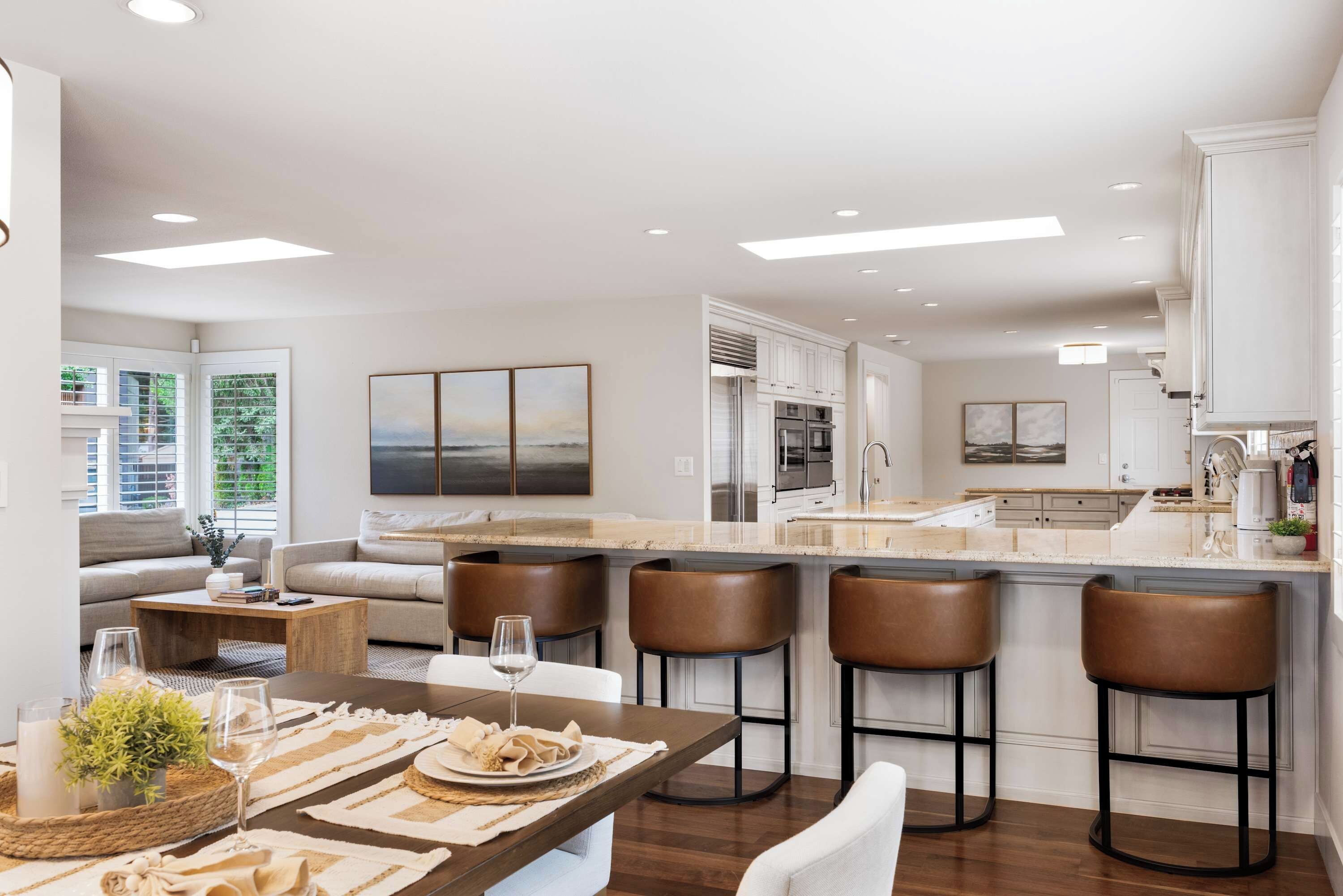 A modern kitchen with a central island, bar stools, and a dining area with a table set for two.